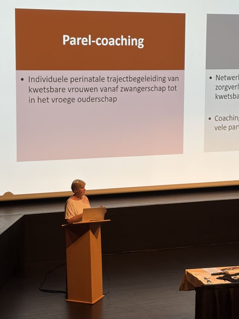 Spreekster achter een spreekgestoelte, met op het scherm een dia over Parel-coaching.