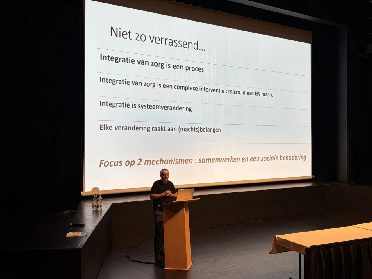 Spreker achter een spreekgestoelte, met op het scherm een dia over integratie van zorg.