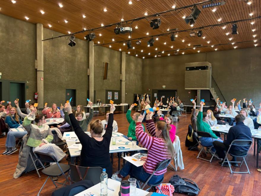 Deelnemers aan de werktafels steken een kaartje in de lucht.
