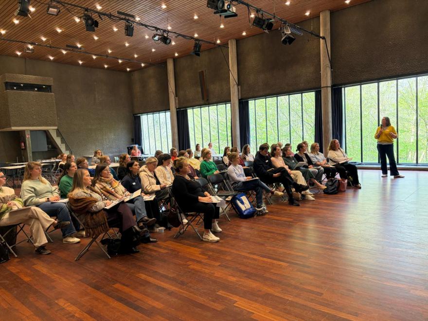 Een zaal vol deelnemers luistert naar een spreekster tijdens de netwerknamiddag van NEST.